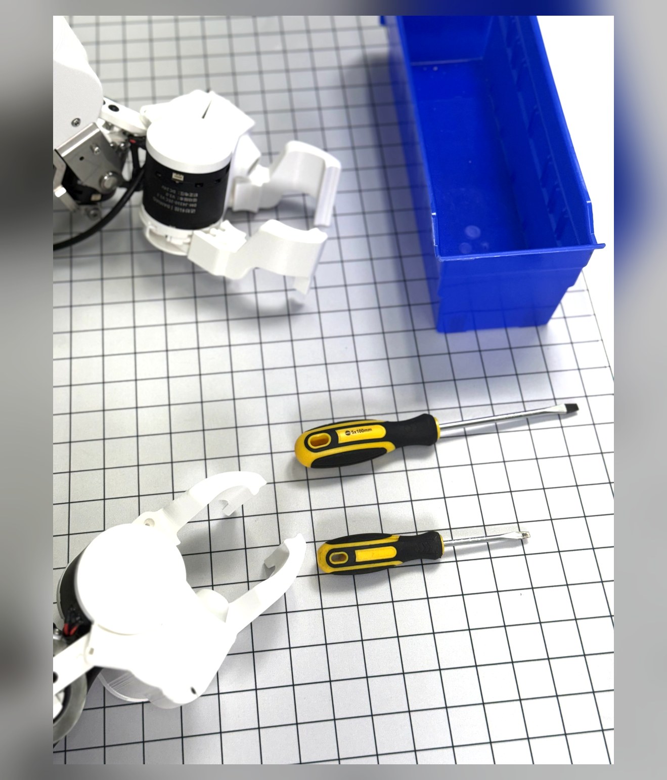 Yuri gripper manipulating tools over a gridded workspace with a parts bin